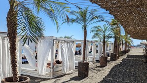 A beachside resort with palm trees, shaded cabanas, and a sandy walkway. - Luxury villa for 8 with infinity pool and panoramic sea views (Sayalonga)