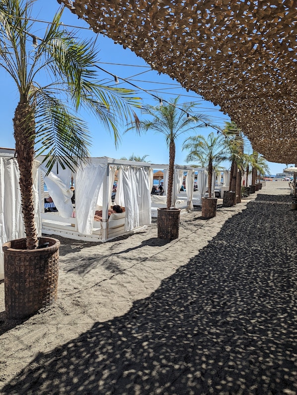 Un complexe hôtelier en bord de mer, avec des palmiers, des cabanons ombragés et une promenade bordée de sable.