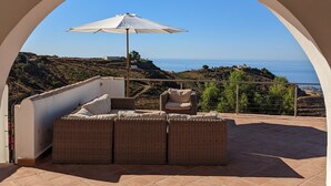 A covered outdoor seating area with a view of the sea and hills. - Luxury villa for 8 with infinity pool and panoramic sea views (Sayalonga)