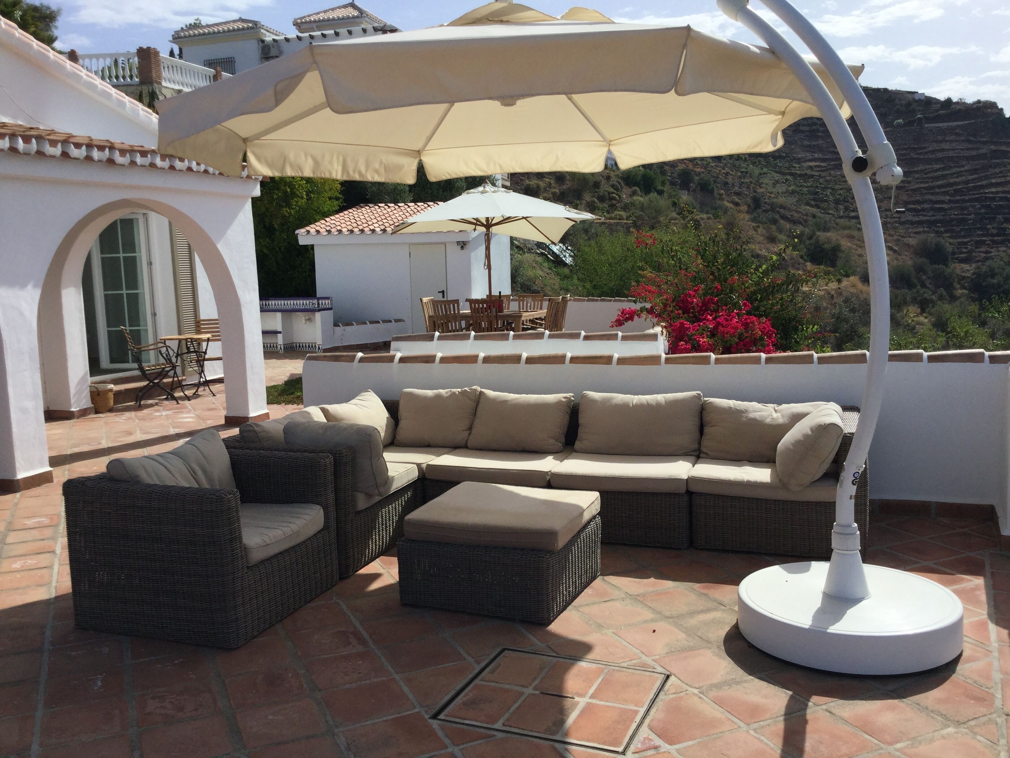 Een terras met een bank, stoelen en een tafel onder een grote parasol.