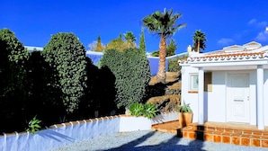 A white building with a tiled roof, a door, and a window. There are plants and a palm tree in front of the building. - Luxury villa for 8 with infinity pool and panoramic sea views (Sayalonga)