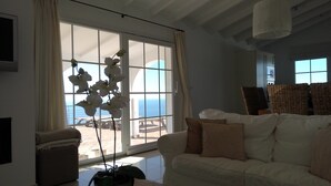 A living room with a large window, a white sofa, and a potted orchid. - Luxury villa for 8 with infinity pool and panoramic sea views (Sayalonga)