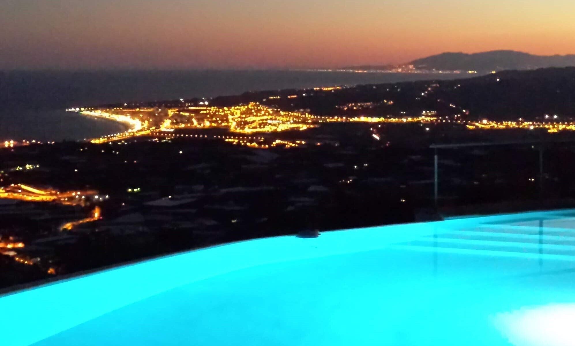A nighttime view of a coastal city with illuminated streets and a pool area.