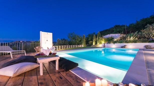 Un espace aménagé au bord de la piscine, avec une terrasse en bois, des chaises longues et une table décorée de bougies.