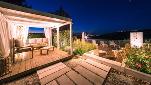 Une terrasse en bois avec des sièges extérieurs, un espace couvert avec un canapé et une vue sur la ville la nuit.