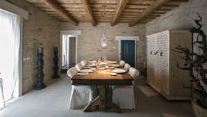 Une salle à manger avec une table en bois dressée pour six personnes, un mur en briques au style rustique et un plafond en bois avec des poutres apparentes.