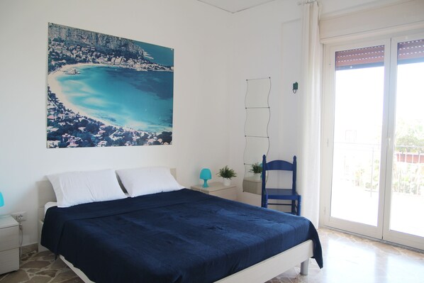 A bedroom with a bed, a nightstand, a chair, a window, and a painting of a coastal scene. - Villa Tea - Beautiful sea view (Palermo)