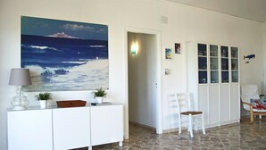 Ein Zimmer mit Steinboden, einem weißen Schrank mit Lampe, einem Sessel und einem Schrank mit Glastüren.