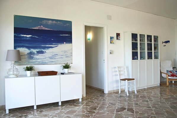 A room with a stone floor, a white cabinet with a lamp, a chair, and a cabinet with glass doors. - Villa Tea - Beautiful sea view (Palermo)