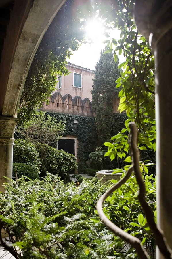 A courtyard with a building, greenery, and a stone archway.