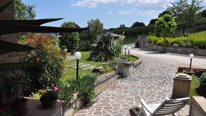 Un chemin de pierre mène à un banc situé dans un jardin aménagé, agrémenté de plantes en pot et d’une statue.