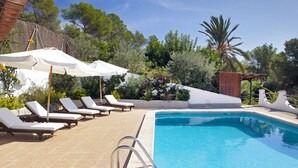 A pool area with lounge chairs and umbrellas, surrounded by greenery and a wooden pergola. - Authentic Ibizan Charm in the Heart of the Island (Santa Eulalia des Riu)