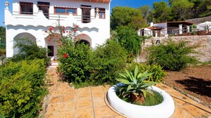 A white building with a tiled roof, a stone pathway, and a garden with various plants. - Authentic Ibizan Charm in the Heart of the Island (Santa Eulalia des Riu)