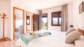 A bedroom with a bed, a mirror, a window with curtains, a wooden headboard, and a door leading to another room. - Authentic Ibizan Charm in the Heart of the Island (Santa Eulalia des Riu)