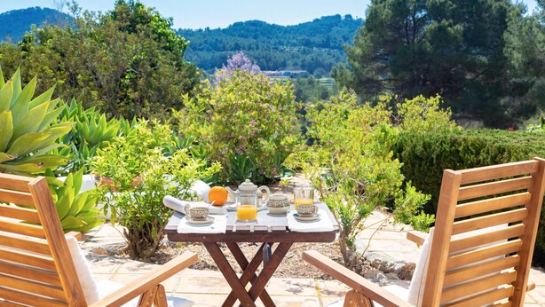 A wooden table with a view of a mountainous landscape, surrounded by greenery and a clear sky. - Authentic Ibizan Charm in the Heart of the Island (Santa Eulalia des Riu)