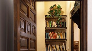 Een smalle gang met een houten deur, een boekenplank vol boeken en een rieten mand.