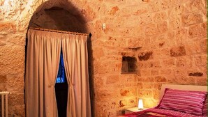 Une pièce avec un mur en pierre, un lit avec un oreiller à rayures et une fenêtre avec des rideaux.