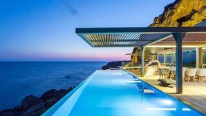 Une piscine à débordement moderne offrant une vue sur l’océan au crépuscule.