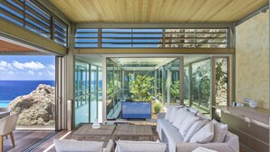 Un intérieur moderne avec un mur en verre, un plafond en bois et un canapé placé face à un téléviseur.