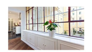 Une pièce avec une grande fenêtre, un meuble blanc avec des tiroirs et une plante en pot posée sur le rebord de la fenêtre.