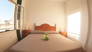 A neatly made bed with a green plush toy in the center, wooden headboard, and two bedside tables with lamps. - Apartment next to the beach with free Wifi, SAT TV, sea views (Gran Tarajal - Fuerteventura)