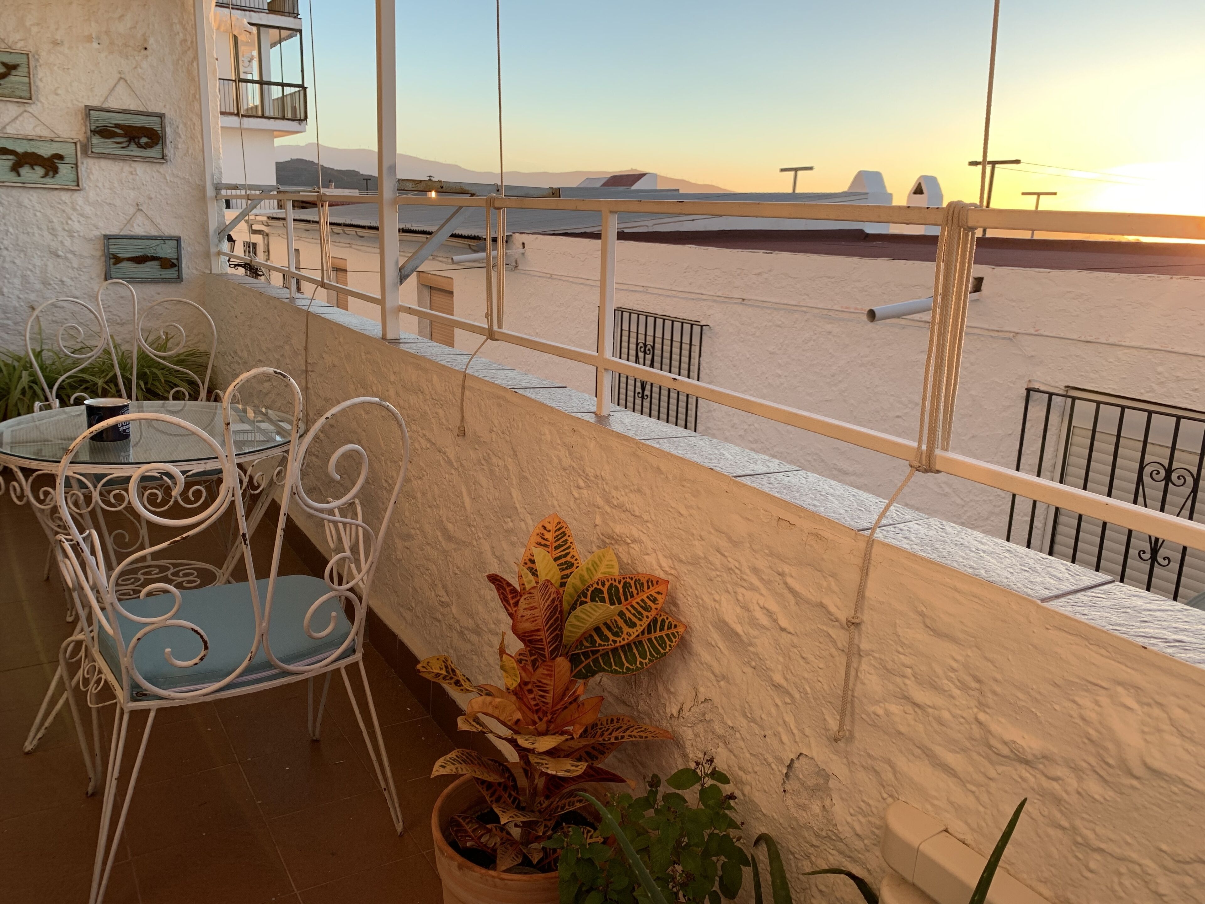 A balcony with a table and chairs, a potted plant, and a view of the beach and mountains.