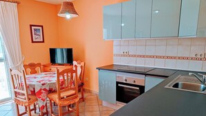 Una cocina compacta con comedor, que incluye un televisor, sillas de madera y un lavamanos moderno.