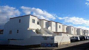 Una hilera de edificios blancos con tejados de tejas, un letrero y coches aparcados.