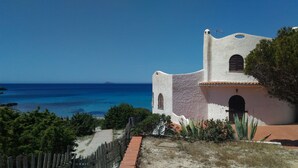 A coastal building with a white facade, a wooden fence, and a view of the ocean. - VILLA WITH PRIVATE GARDEN NEAR THE SEA (Porto Pino)