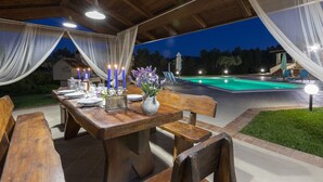 Un espace extérieur aménagé pour les repas, avec une table en bois dressée pour un repas, entourée de chaises, et une piscine en arrière-plan.