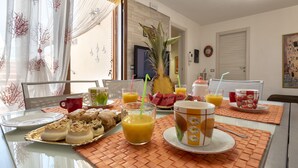 Una mesa de desayuno con diferentes alimentos y bebidas, una planta y vistas al exterior.