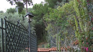 A curved outdoor pathway with terracotta tiles, a metal gate, and a stone wall.