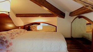 A bedroom with a vaulted ceiling, wooden beams, a bed with floral bedding, and a nightstand.