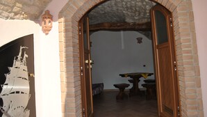 Un arco de ladrillo con un vano arqueado y una puerta de madera, que da paso a una habitación con suelo de baldosas y una mesa con sillas.