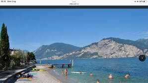 Una playa con agua cristalina, gente nadando y caminando, y montañas al fondo.