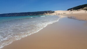 A beach with clear turquoise water, sandy shore, and a hilly landscape in the background. - Bahia del Mar  with dream views ,climatisation and wi-fi (Casares)