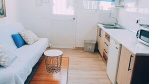 A compact living space with a kitchenette, a bed with patterned pillows, a small round table, and a red pendant light.
