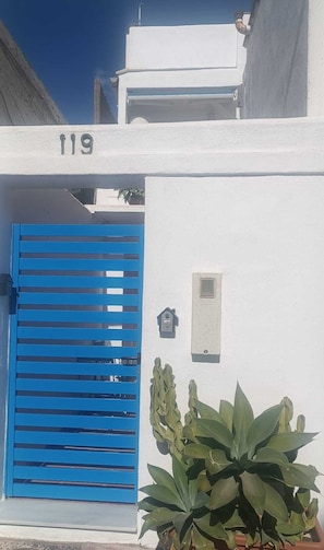 Un bâtiment blanc avec une porte bleue à volets, le numéro « 119 » au-dessus de la porte et une petite boîte aux lettres fixée au mur.
