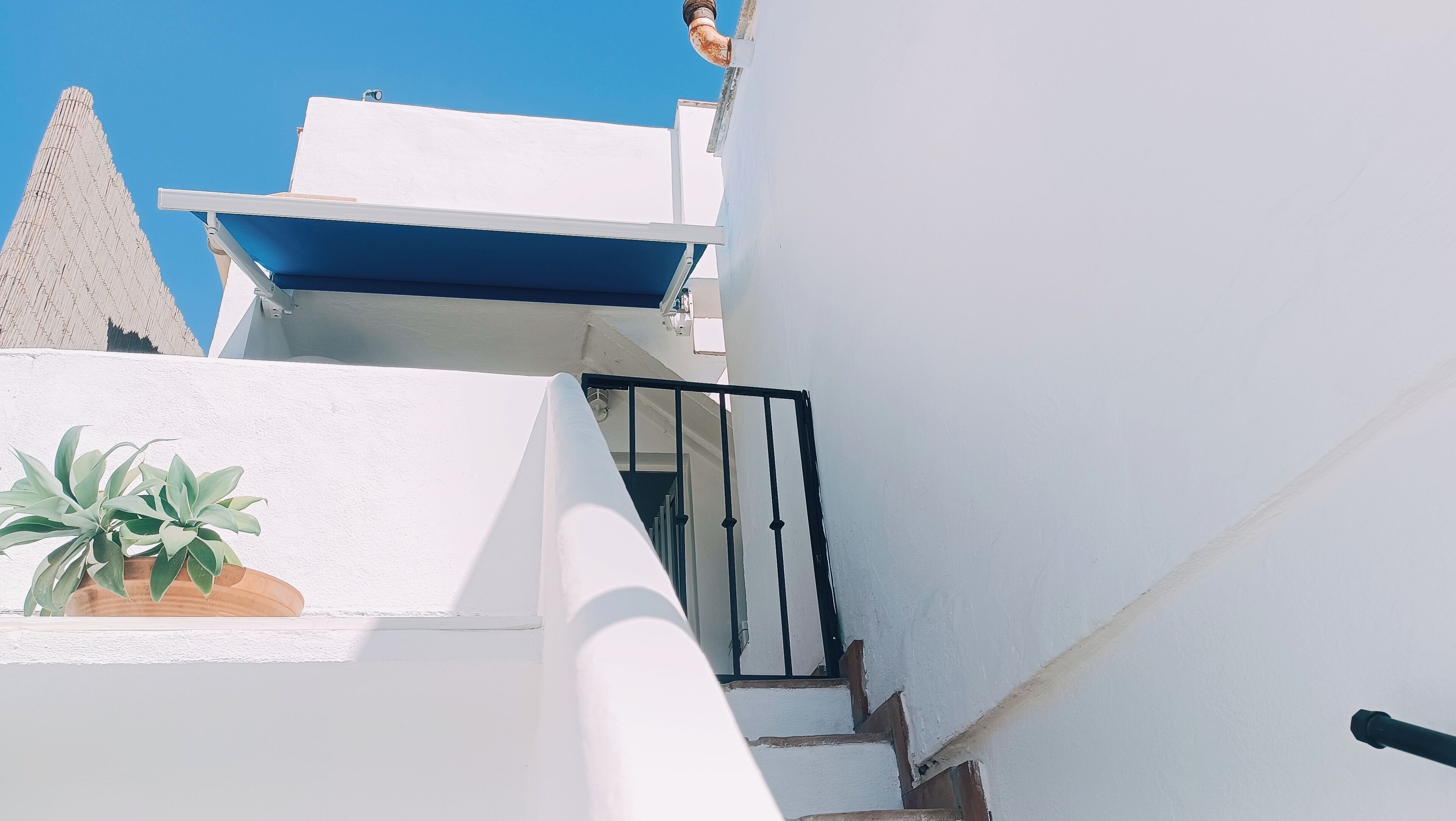 Un escalier étroit mène à un bâtiment blanc surmonté d’une marquise bleue.