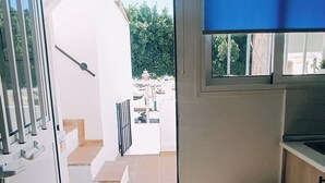 A room with a sliding door leading to a balcony, a small kitchen area, and a view of the outdoors.