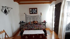 Una camera da letto con un letto a struttura metallica, una coperta colorata, un baule di legno, un tavolino con una lampada e una sedia.