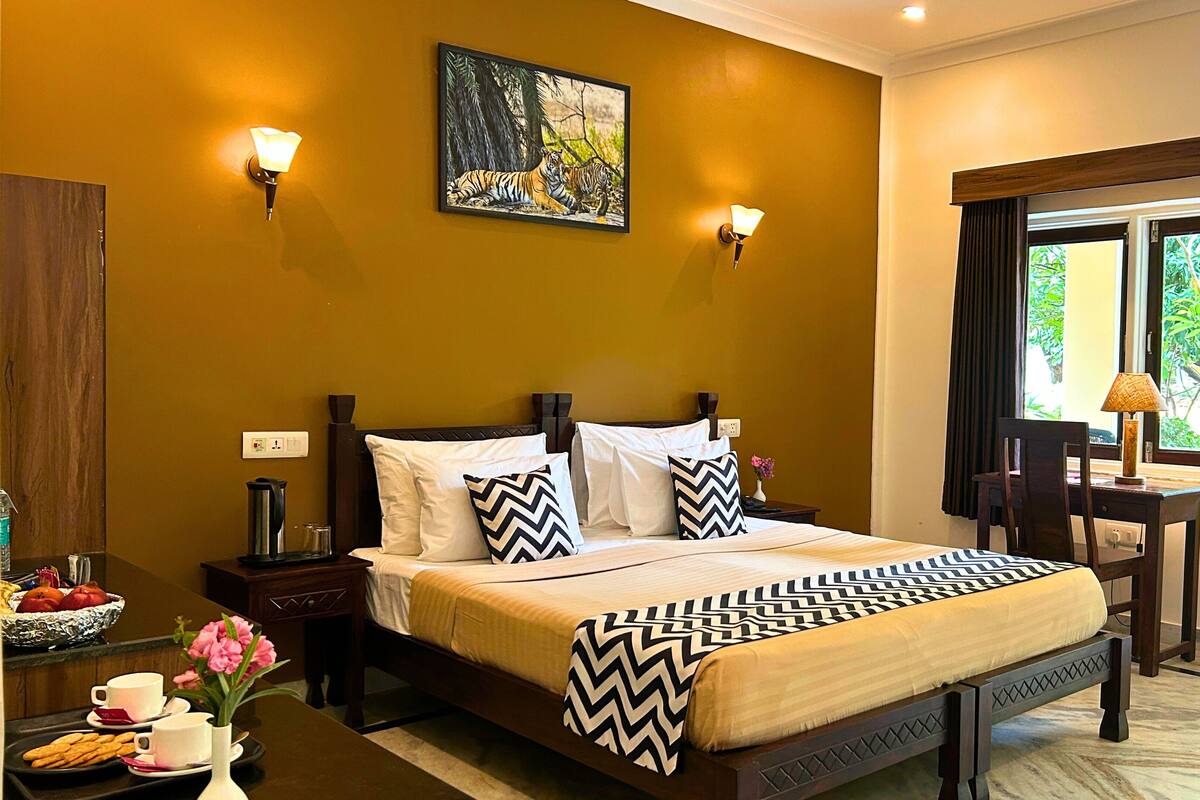 Une chambre d’hôtel avec un lit, deux appliques murales, une fenêtre avec des rideaux, une table de chevet, un plateau avec des en-cas et un tableau au mur.