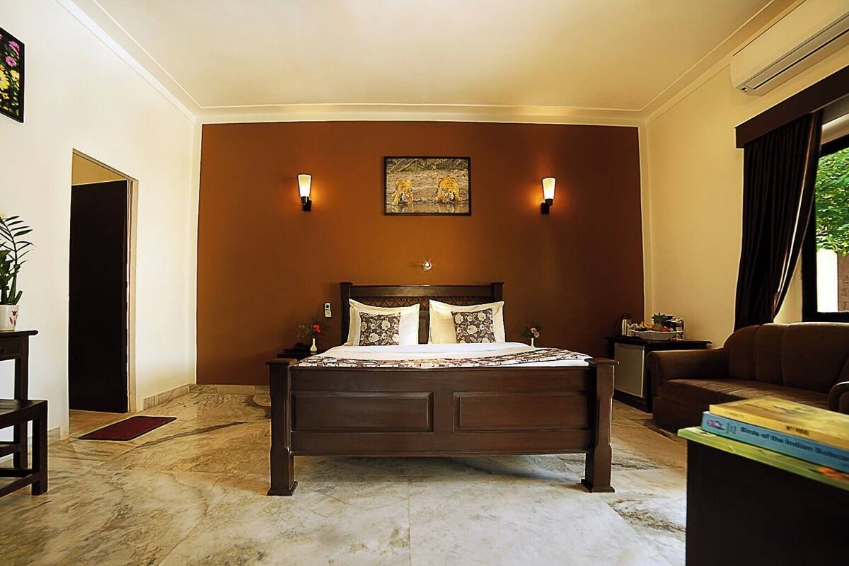 Une chambre avec un grand lit, deux lampes fixées au mur, un tableau au-dessus du lit, un canapé et une fenêtre avec des rideaux.