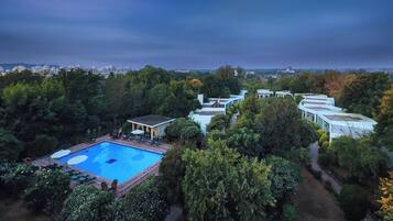 Zona de piscina con sillones de descanso, rodeada de exuberante vegetación y vistas a edificios lejanos.