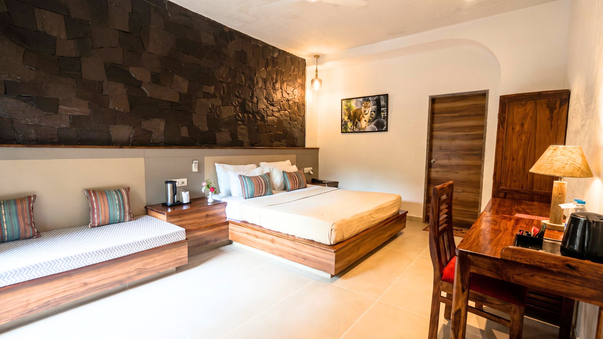 A modern bedroom with a stone accent wall, a bed with multiple pillows, a bedside table with a lamp, and a wooden desk with a chair.