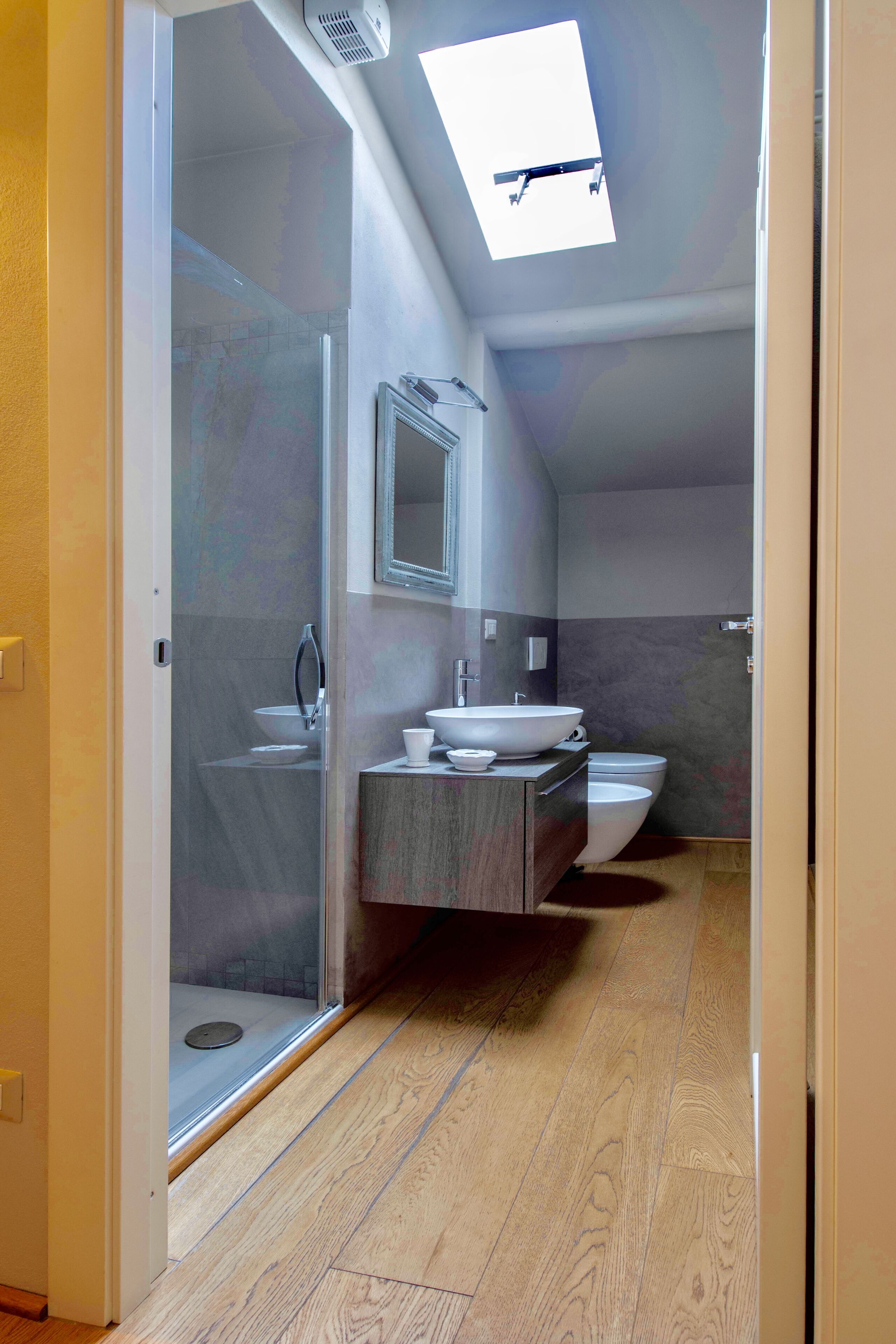A modern bathroom with a skylight, a glass shower enclosure, a vanity with a sink, and a toilet.