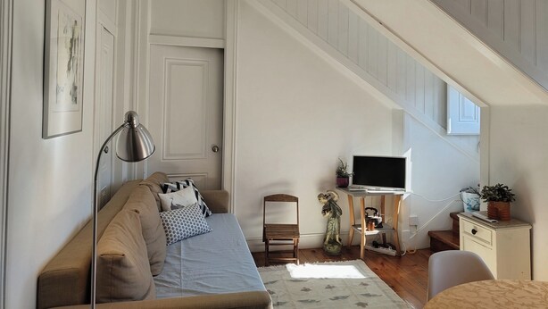 A loft-style bedroom with a sloped ceiling, a sofa, a TV, a desk, and a small statue. - Sunny 2BR - Av. D. Carlos I, Lisbon (São Bento) (Lisboa)