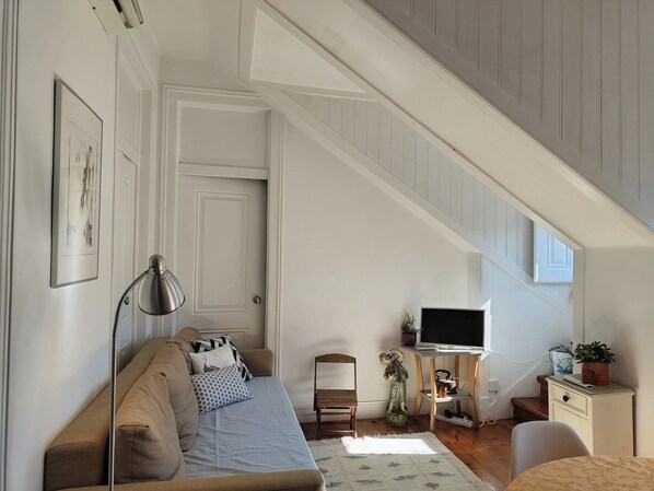 A loft-style bedroom with a sloped ceiling, a sofa, a TV, a desk, and a small statue.