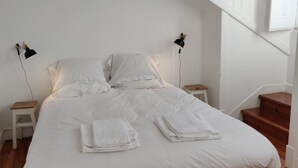 A neatly made bed with white linens and folded towels, two bedside lamps, and a wooden nightstand. - Sunny 2BR - Av. D. Carlos I, Lisbon (São Bento) (Lisboa)