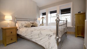 A neatly arranged bedroom with a bed, two bedside tables, a nightstand, a wooden wardrobe, and a window with a view. - Relax in the Heart of Bronte Country (Haworth)